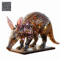 A glass animal sculpture of an aardvark on a rectangular base, shown against a plain white background. The sculpture is made of many reflective, metallic polygonal pieces in warm gold, bronze, and brown tones, with pinkish inner ears.